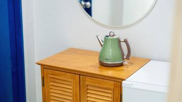 A green kettle on a wooden cabinet in a bathroom.