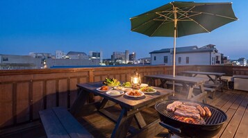Um terraço no telhado com churrasqueira, mesa de jantar e guarda-sol.