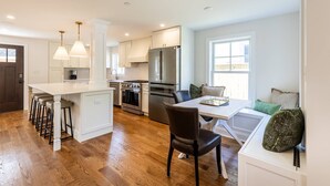 A modern kitchen with a central island, bar stools, a dining table with chairs, and a seating area with cushions. - Walk Everywhere From Eastport Cape Cod with Gourmet Kitchen (Annapolis)