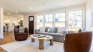 A spacious living room with a sofa, two armchairs, a coffee table, and large windows. - Walk Everywhere From Eastport Cape Cod with Gourmet Kitchen (Annapolis)