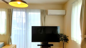 Un soggiorno con televisione a schermo piatto, un tavolino in legno, una pianta in vaso e una lampada a soffitto.