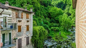 A stone building with multiple windows and balconies, surrounded by lush greenery and a flowing stream. - Lovely apartment for 3 people with TV and balcony (Nesso)
