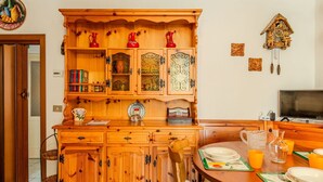 A wooden kitchen with a built-in cabinet, a dining table with a chair, and a wall-mounted cuckoo clock. - Lovely apartment for 3 people with TV and balcony (Nesso)