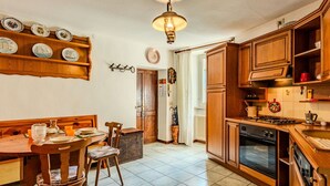 A kitchen with wooden cabinets, a stove, and a dining area with chairs and a table. - Lovely apartment for 3 people with TV and balcony (Nesso)