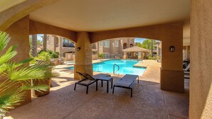 An outdoor pool area with lounge chairs and a pool table, surrounded by a covered patio with a view of the pool and buildings in the background. - Luxury 2-bedroom condo in Scottsdale! (Scottsdale)