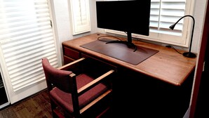 A wooden desk with a computer monitor and keyboard, a chair, and a window with blinds. - Mountain View • Pool House • BBQ (Chino Hills)