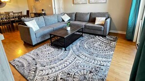 Un salon comprenant un canapé d’angle, une table basse, un tapis à motifs et un ventilateur de plafond.