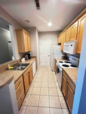 A kitchen with wooden cabinets, a stainless steel sink, a microwave, a stove, and a refrigerator. - Cozy condo in Villages of Five Points, Lewes (Lewes)