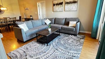 A living room with a sectional sofa, a coffee table, a patterned rug, and a ceiling fan.