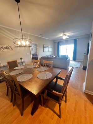 A dining area with a wooden table and chairs, a ceiling fan, and a wall with a 'gather' sign. - Cozy condo in Villages of Five Points, Lewes (Lewes)