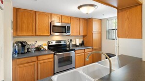 A kitchen with wooden cabinets, a stainless steel microwave, a built-in oven, a sink, and a coffee maker.