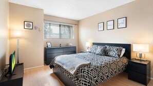 A bedroom with a bed, bedside tables, a dresser, a TV, and a window with blinds.