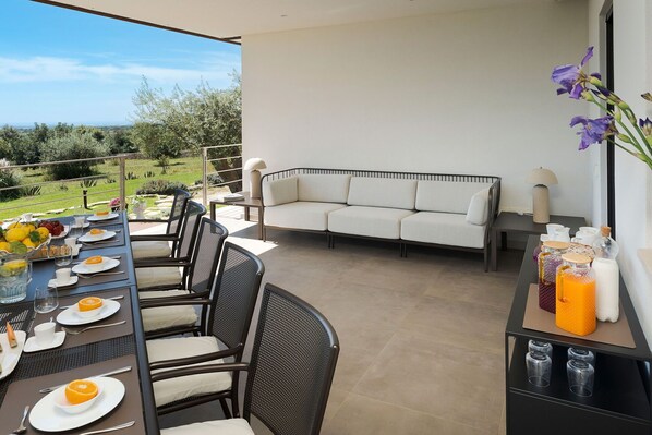 A balcony with a dining table set for breakfast, a sofa, and a view of the landscape.