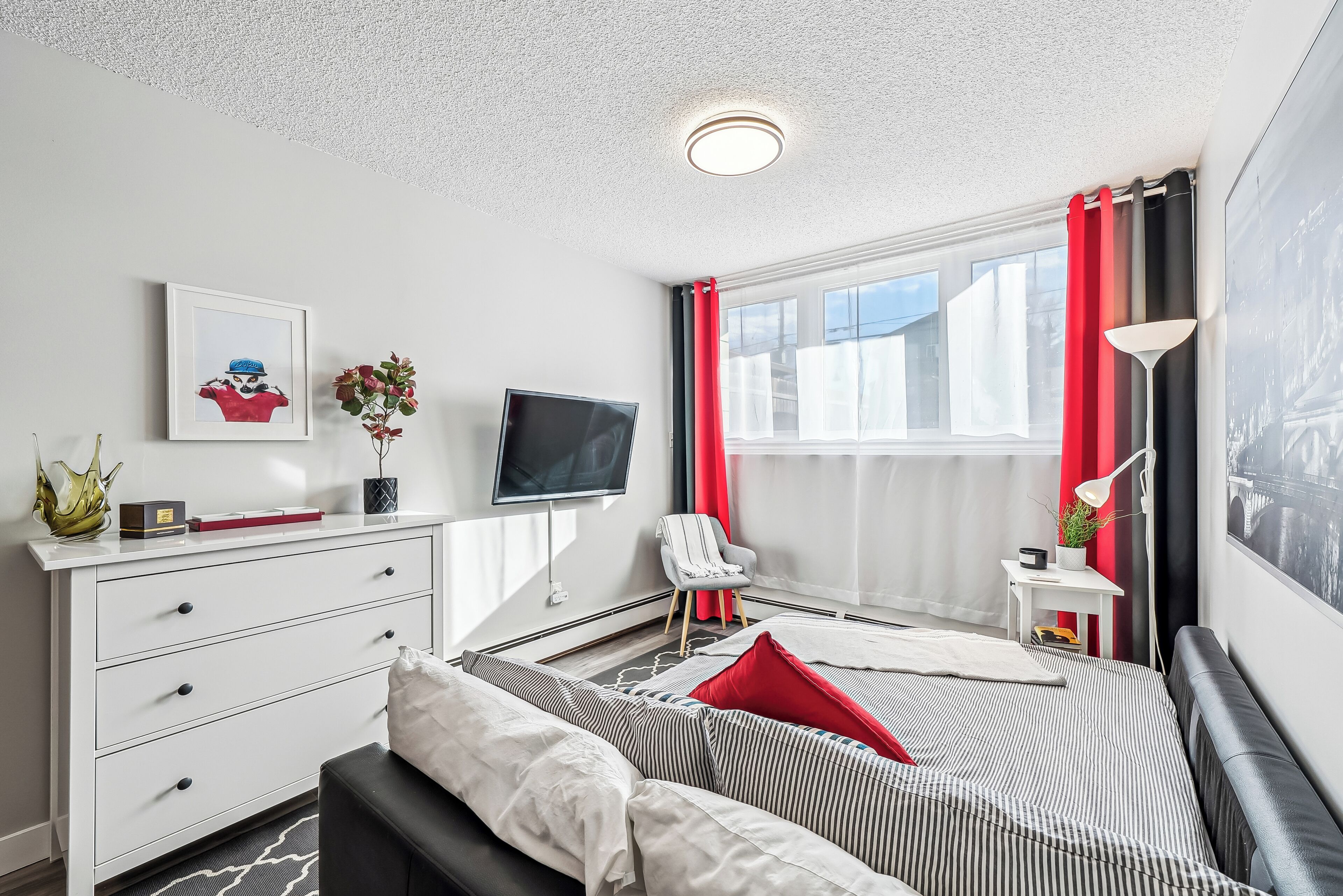 Een moderne slaapkamer met een bed, een televisie, een bureau en een raam met gordijnen.