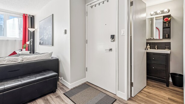 Une chambre à coucher moderne avec un canapé en cuir noir, une porte blanche et une petite salle de bain dotée d’un miroir et d’un lavabo.