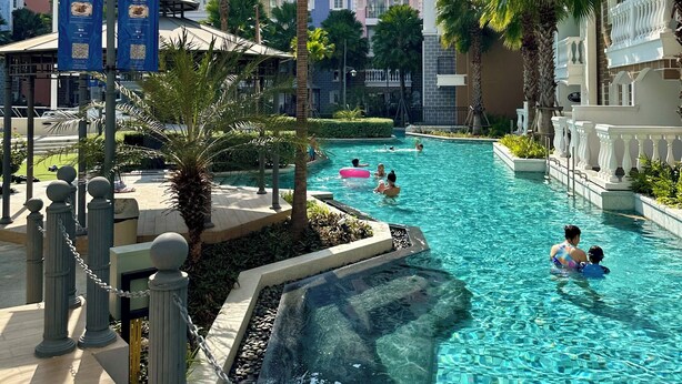 A swimming pool surrounded by palm trees and multi-story buildings.