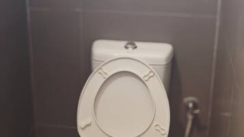 A standard toilet with a closed seat and lid, a visible flush handle, and a wall-mounted flush button.