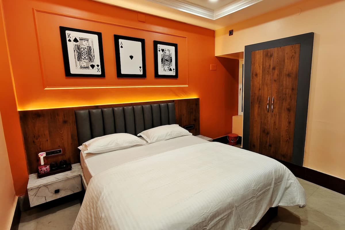 A modern bedroom with a large bed, a nightstand, a wardrobe, and three framed playing cards on the wall.
