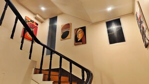 A staircase with a black handrail and beige walls, featuring three artworks: a colorful abstract, a geometric design, and a minimalist face. - The Saanjh Hotel (Angul)