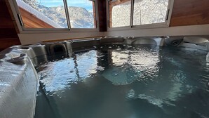 A hot tub with a view of snow-covered mountains through large windows.