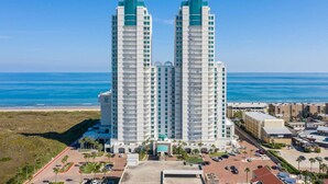 Ein hoch aufragendes Hotel mit Blick auf den Strand, das zwei markante Türme mit Balkonen, einen Parkplatz und einen angelegten Eingangsbereich zeigt.