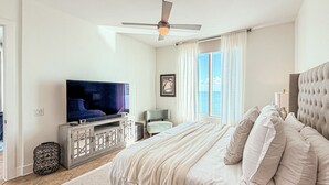 Ein Schlafzimmer mit einem großen Bett, einem Fernseher, einem Deckenventilator und einem Fenster mit Vorhängen.
