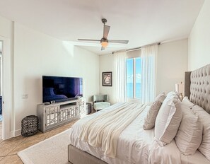 Una camera da letto con un letto grande, una televisione, una ventola a soffitto e una finestra con tende.