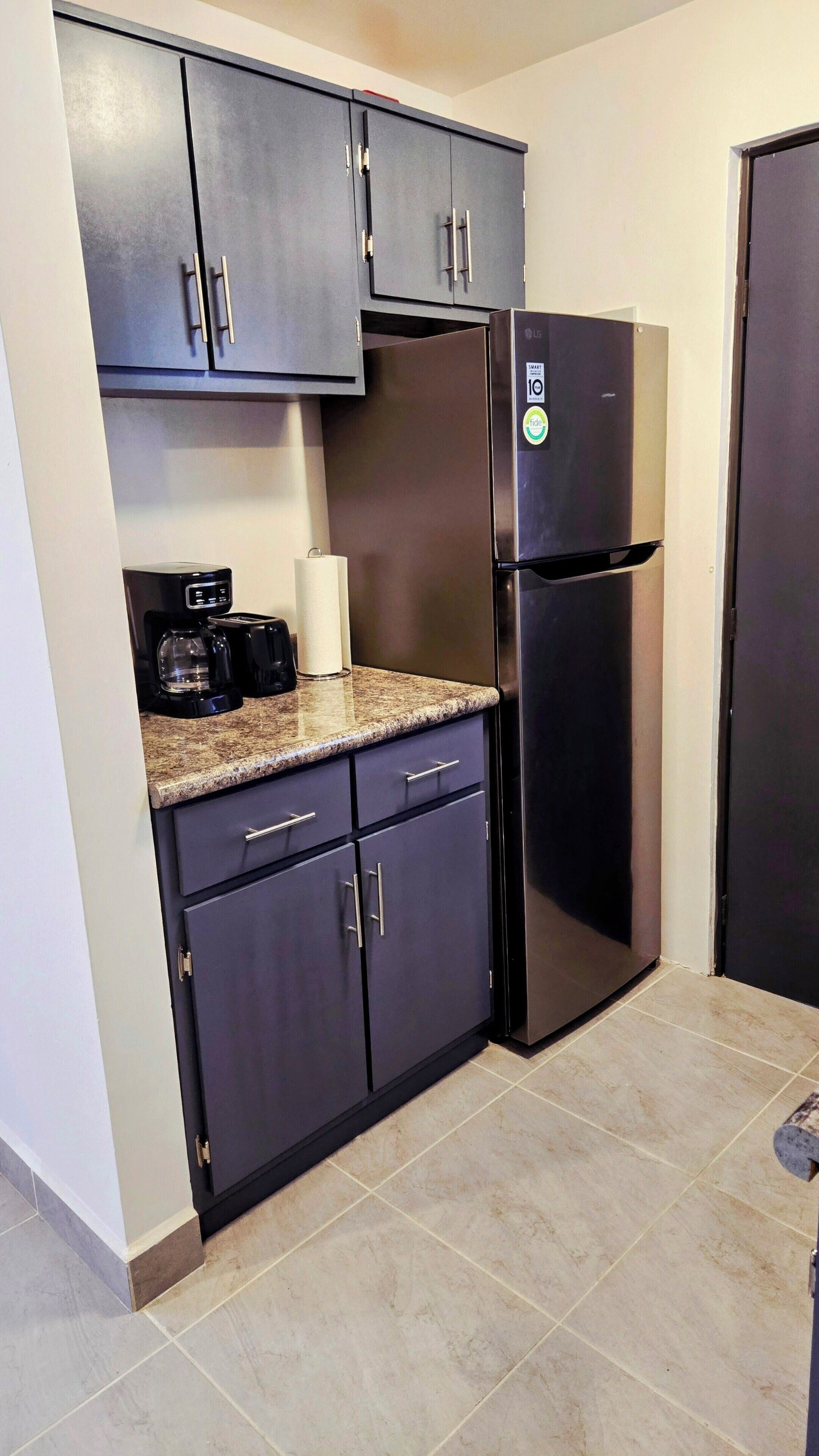 A compact kitchen with dark cabinets, a stainless steel refrigerator, a coffee maker, and a toaster.