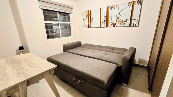 A compact room with a sofa bed, a small table, and a window. - Charming Corner House 3br 2bath w/garage, Pets OK (Ensenada)