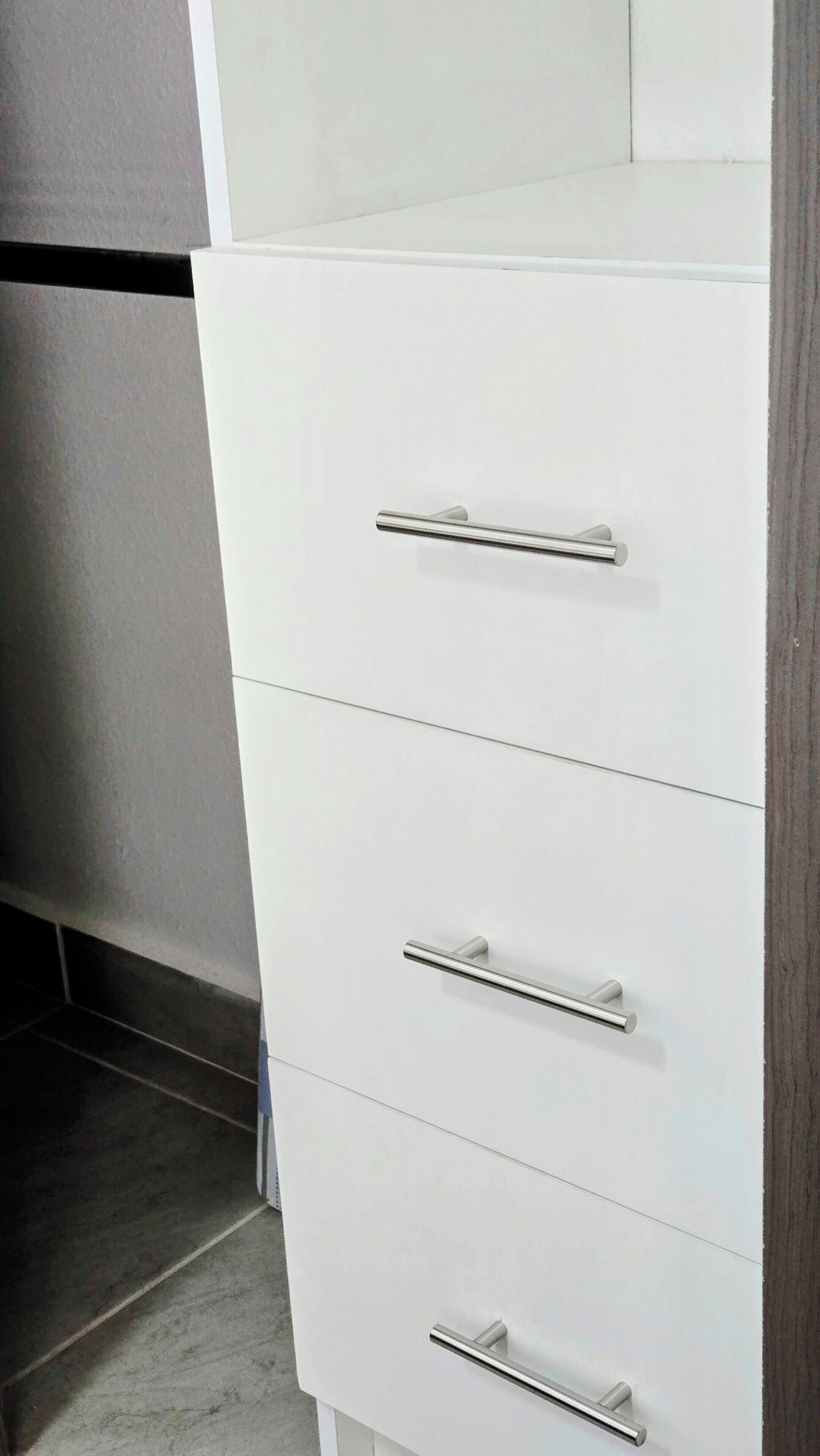 A white cabinet with three drawers and two handles.