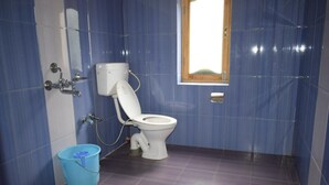 Un baño con paredes de azulejos azules, un inodoro blanco, un balde azul y una ventana con vistas.