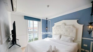 A bedroom with a large bed, a television on a stand, and a window with a view of buildings. - E8 - 2bedroom french style beautiful pool view Pattaya Seven seas cote d azur (Tambon Na Chom Thian)