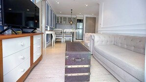 A modern living room with a sofa, a television, and a dining area with chairs and a table. - E8 - 2bedroom french style beautiful pool view Pattaya Seven seas cote d azur (Tambon Na Chom Thian)