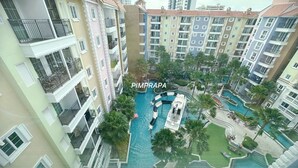 A multi-story residential building with balconies, a central swimming pool, and surrounding greenery. - E8 - 2bedroom french style beautiful pool view Pattaya Seven seas cote d azur (Tambon Na Chom Thian)