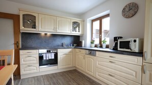 A kitchen with light-colored cabinets, a microwave, an oven, and a window with a view. - Apartment no. 3 with mountain view, 62m², modern furnishings and very large south/east-facing balcony (Übersee)