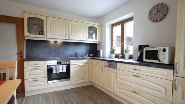 A kitchen with light-colored cabinets, a microwave, an oven, and a window with a view. - Apartment no. 3 with mountain view, 62m², modern furnishings and very large south/east-facing balcony (Übersee)