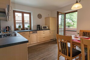 A kitchen with wooden cabinets, a microwave, a coffee maker, and a dining area with a table and chairs. - Apartment No. 3 with a mountain view, 62 m², modern furnishings, and a large south/east-facing balcony (Übersee)