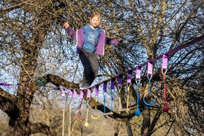 Una persona sobre un pont de corda, amb arnes de seguretat i cintes de colors.
