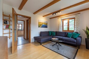 A modern living room with a sectional sofa, a coffee table, and a view of a lake through a window. - Apartment No. 3 with a mountain view, 62 m², modern furnishings, and a large south/east-facing balcony (Übersee)