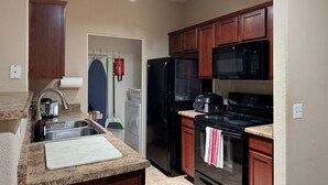 Une cuisine moderne dotée de plans de travail en granit, d’un réfrigérateur noir, d’un four à micro-ondes et d’une cuisinière.