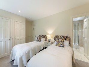 Une chambre d’hôtel avec deux lits, du linge de lit blanc, une table de chevet avec une lampe et un espace douche.