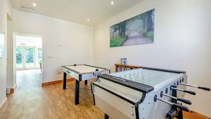 A room with two foosball tables, a painting of a forest path, and a door leading to a balcony.