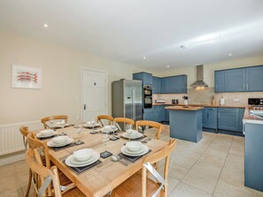 A modern kitchen with blue cabinets, a central island, and a dining area with wooden chairs and a table set for six.