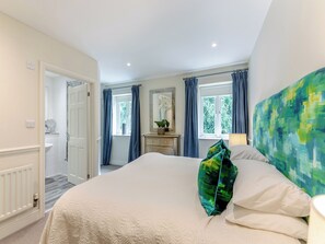 A bedroom with a bed, a dresser, a window with curtains, a mirror, and a painting on the wall.