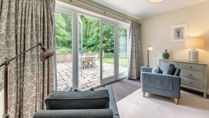 A room with a sofa, a lamp, a side table with a vase, a picture on the wall, and a view through a glass door to an outdoor area with a table and chairs.