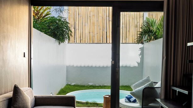 A modern living room with a glass door leading to a backyard with a pool and bamboo fence. - Solis Loft Villa by Betterplace (Canggu)