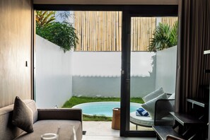 Ein modernes Wohnzimmer mit Glastür, die zu einem Garten mit Pool und Bambuszaun führt.