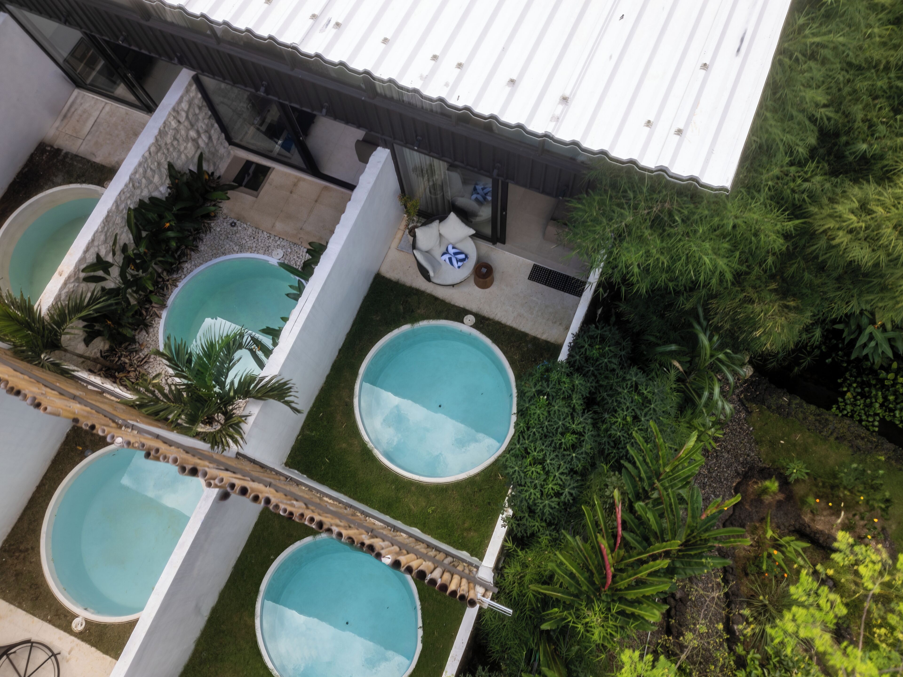 Un área de piscina en la azotea con tres piscinas, rodeada de follaje y un porche cubierto.