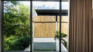 A room with large windows offering a view of a bamboo fence and greenery outside. - Solis Loft Villa by Betterplace (Canggu)