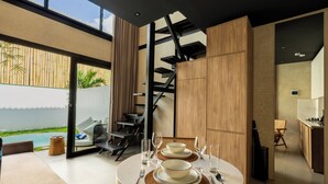 A modern dining area with a round table set for two, a staircase, and a view of the ocean. - Solis Loft Villa by Betterplace (Canggu)